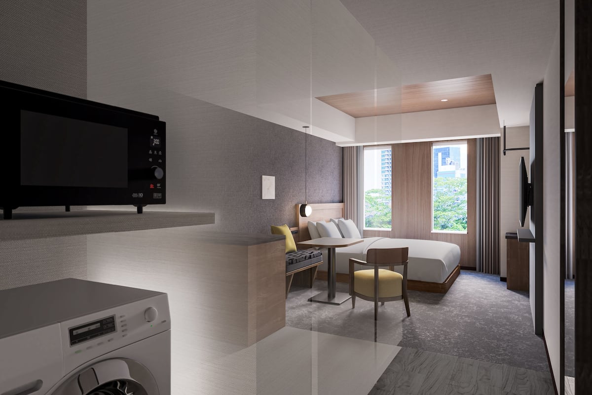 Una habitación de hotel moderna con televisión de pantalla plana, lavadora, cama con vistas a la ciudad y zona de comedor.