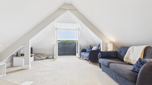 Een ruime zolderkamer met een hoge plafond, een ingebouwd bureau, een comfortabele bank en een groot raam met uitzicht op de omgeving.