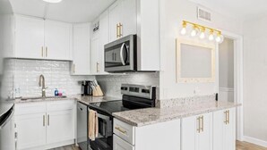 Une cuisine moderne avec des meubles blancs, une cuisinière noire, un four à micro-ondes et un plan de travail agrémenté d’un luminaire.