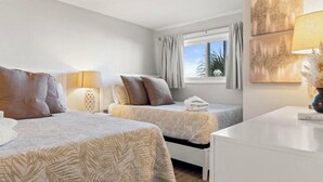 Une chambre d’hôtel avec deux lits, une fenêtre avec des rideaux, une lampe et des œuvres d’art accrochées au mur.