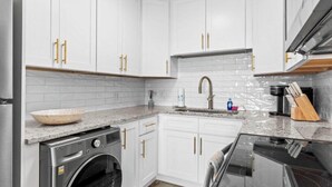 Une cuisine moderne avec des armoires blanches, un lave-linge en acier inoxydable, un comptoir en granit et une hotte de cuisinière en acier inoxydable.