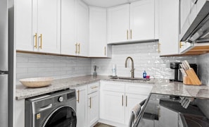 A modern kitchen with white cabinets, a stainless steel washing machine, a granite countertop, and a stainless steel range hood. - Cozy Beachfront 1-Bedroom Condo-Heated Pool & Gulf View-Sleeps 6 (Panama City Beach)