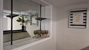 A kitchen with a glass shelf holding wine glasses and a potted plant.