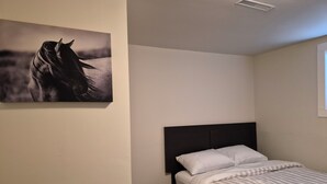 A bedroom with a bed, a headboard, a wall-mounted artwork of a horse, and a window.
