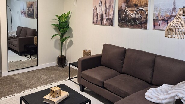 A living room with a brown sectional sofa, a black coffee table, a large mirror, and cityscape artwork on the walls.