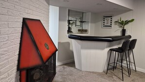A corner room with a white brick wall, a red fireplace, a bar counter, and a seating area with two chairs.