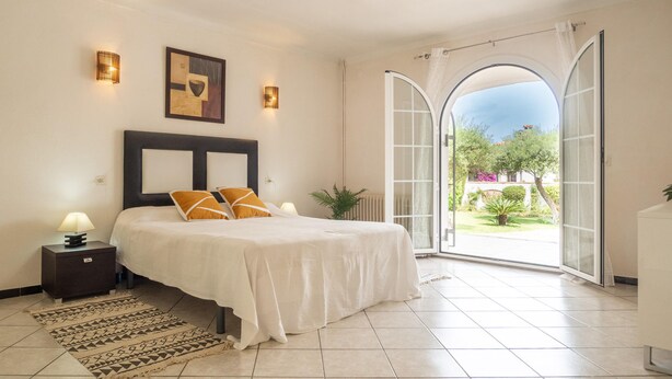 Ein Schlafzimmer mit Bett, Nachttischlampen, einem Teppich und Blick durch eine offene Tür.