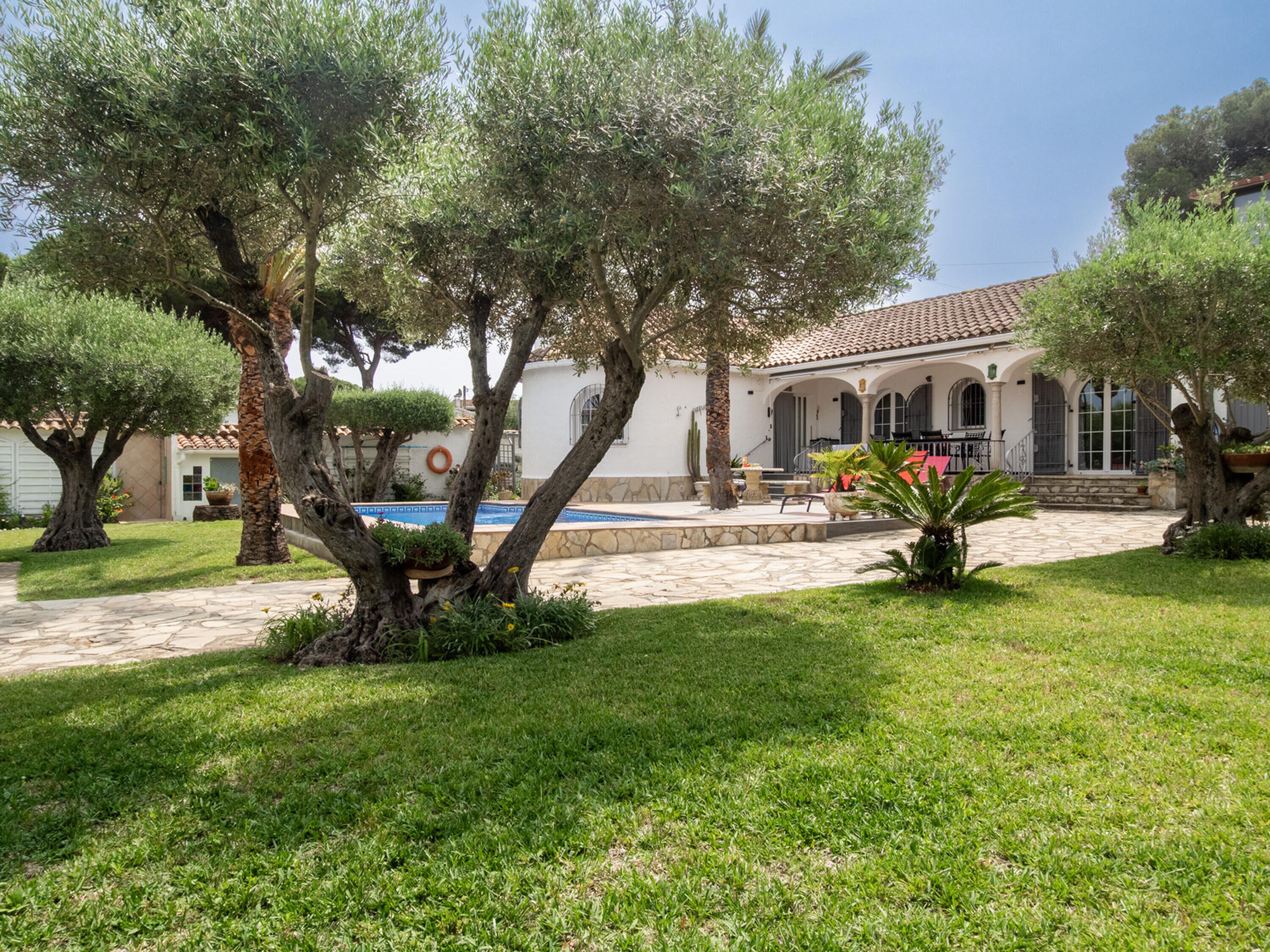 Eine Villa mit Swimmingpool, umgeben von gepflegten Rasenflächen und Bäumen.