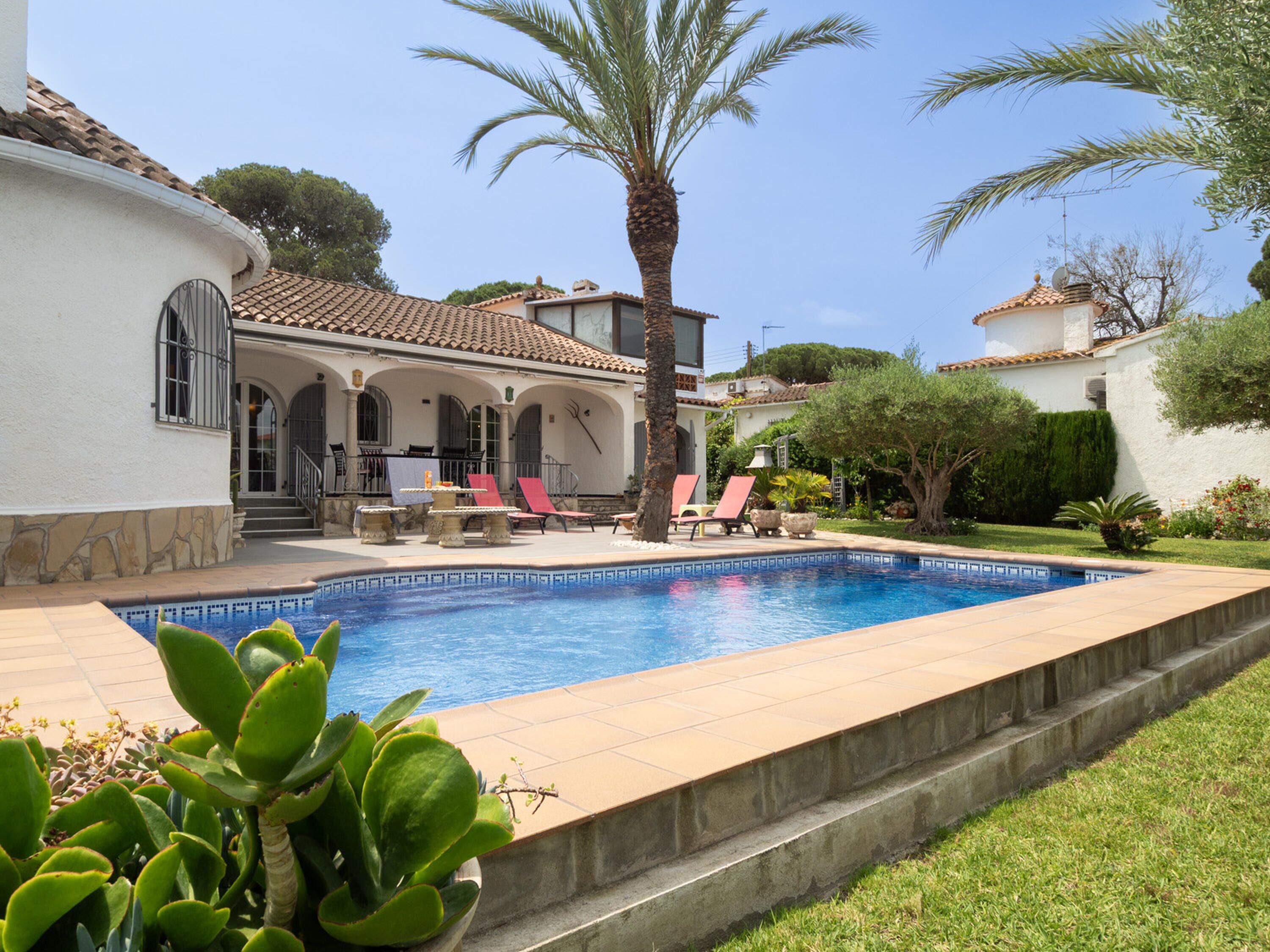Una piscina con sillas de descanso, una palmera y un edificio con techo de tejas.
