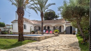 Ein mit Kopfsteinpflaster belegter Innenhof mit einem Pool, Palmen und einem weißen Gebäude mit einem Ziegeldach.