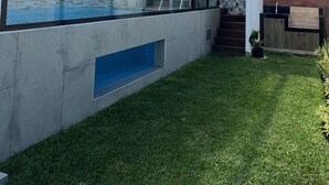Ein moderner Poolbereich im Freien mit Glasverkleidung, einer Steinmauer und einer Rasenfläche.
