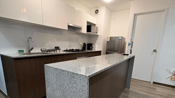 Eine moderne Küche mit weißen Schränken, einer Kochinsel mit Granitplatte, Edelstahlgeräten und einer hängenden Pendelleuchte.