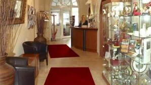 A hotel lobby with a reception desk, a chandelier, a red carpet, and a glass display case with items. - Hotel Schweizer-hof Baden Baden (Baden-Baden)
