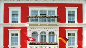 A hotel with a red facade, a balcony with plants, and a sign reading 'HOTEL SCHWEIZER NOF'. - Hotel Schweizer-hof Baden Baden (Baden-Baden)