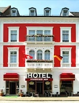 Um hotel com fachada vermelha, uma varanda com plantas e uma placa com a inscrição 'HOTEL SCHWEIZER NOF'.