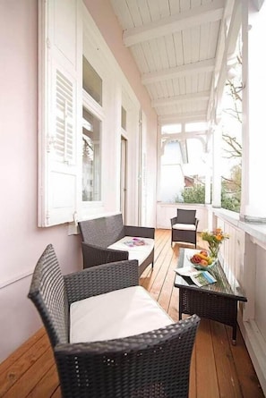Une véranda aménagée avec des meubles en osier, une table garnie de fruits et une vue sur l’extérieur.