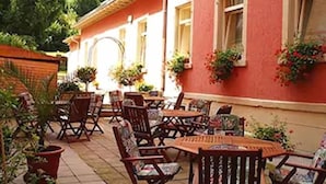 An outdoor patio with wooden tables and chairs, potted plants, and a red building with windows. - Hotel Schweizer-hof Baden Baden (Baden-Baden)