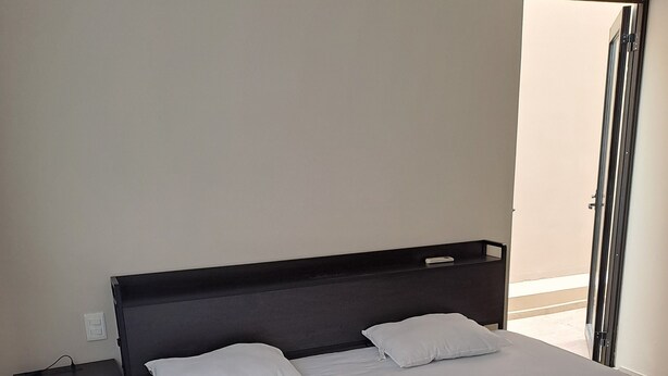 A neatly made bed with white linens, a dark headboard, and a small bedside table with a lamp. - 2-bedroom bed & breakfast in charming Cancun with AC (Cancun)