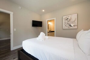 Une chambre à coucher avec un lit, un téléviseur à écran plat, un tableau et une salle de bain visible à travers une porte ouverte.