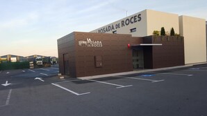 Um estacionamento com vagas demarcadas e um edifício com a placa 'POSADA DE ROCES'.