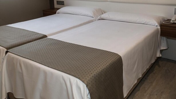 Uma cama de casal com cabeceira, duas mesas de cabeceira e uma janela com cortinas.