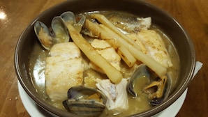 Uma tigela de ensopado de frutos do mar com amêijoas e peixe.