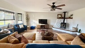 A living room with a fireplace, a ceiling fan, and a television. - Ranchito Robles, Hot Tub • Fire Pit • Wine Country Retreat (Paso Robles)