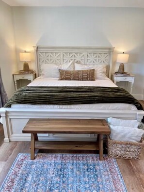 A bedroom with a white bed, a wooden bench, a patterned rug, and two nightstands with lamps. - Ranchito Robles, Hot Tub • Fire Pit • Wine Country Retreat (Paso Robles)