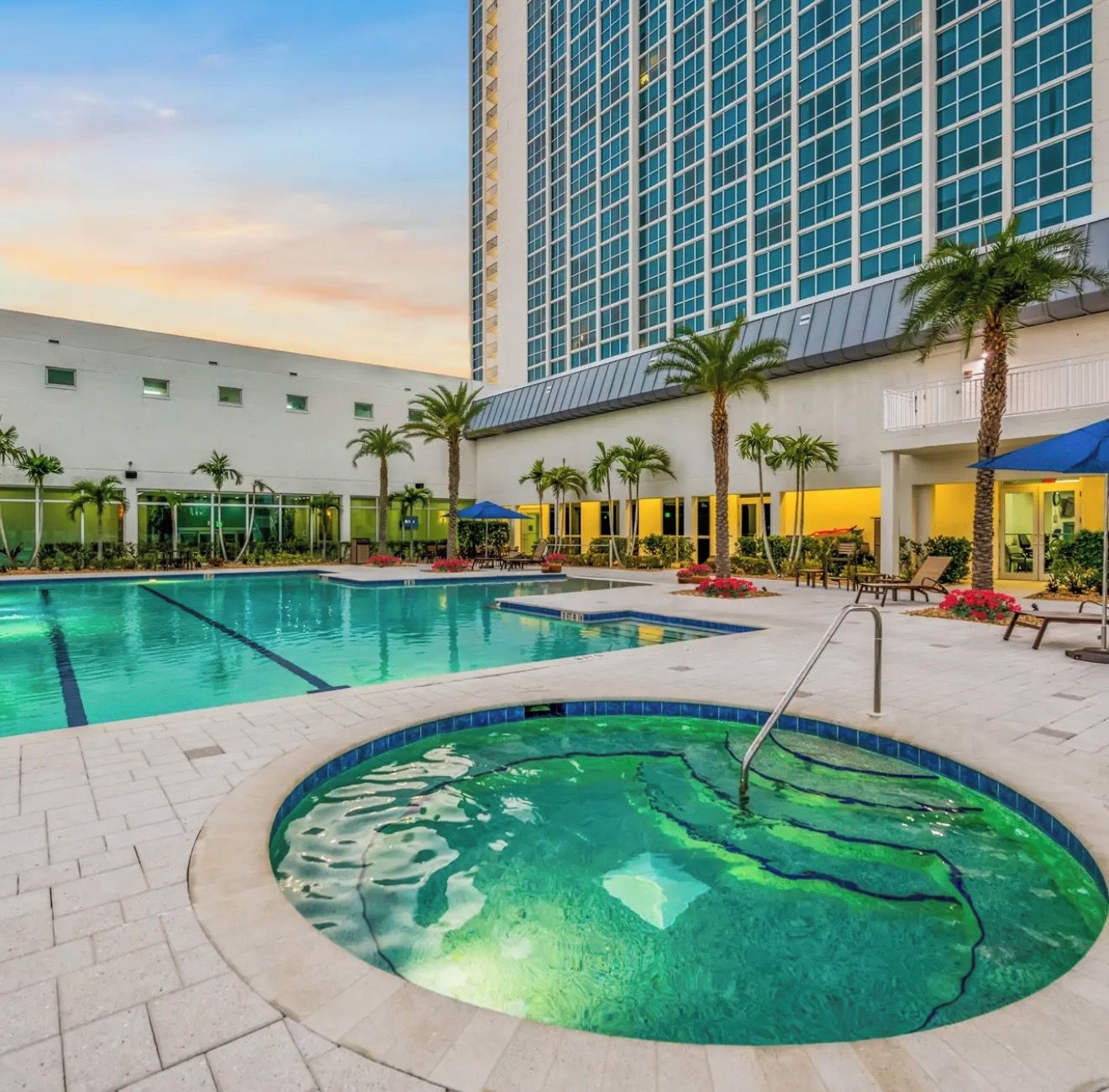 Ein Hotelpoolbereich mit Whirlpool, Palmen und einem großen Gebäude im Hintergrund.