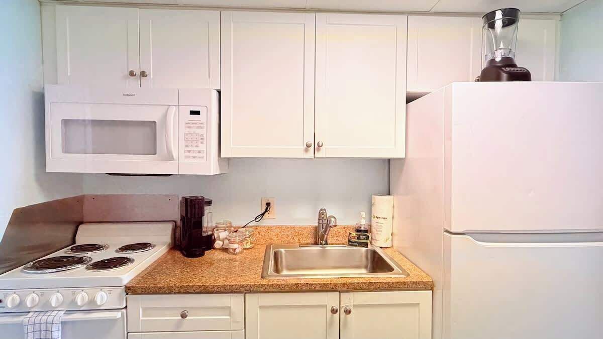 Une cuisine avec des meubles blancs, un four à micro-ondes, une cuisinière, un évier et un mixeur.