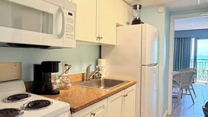 Uma cozinha moderna com armários brancos, fogão, micro-ondas e geladeira.