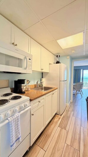 A modern kitchen with white cabinets, a stove, a microwave, and a refrigerator. - Direct Oceanfront 1BR – 3rd Floor Retreat (Myrtle Beach)