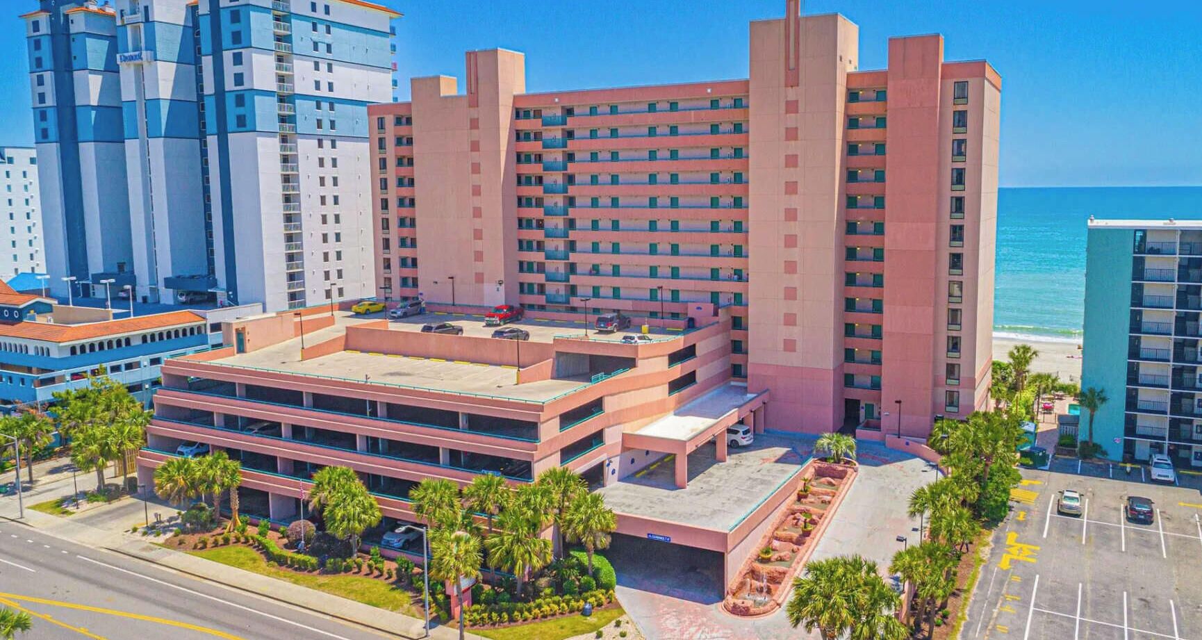 A multi-story hotel with a parking garage, palm trees, and a view of the ocean.