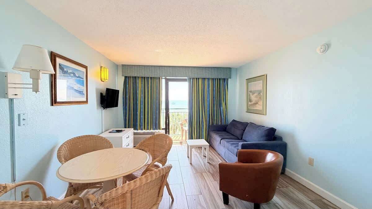 Een kamer met een eettafel, stoelen, een bank, een televisie en een raam met gordijnen.