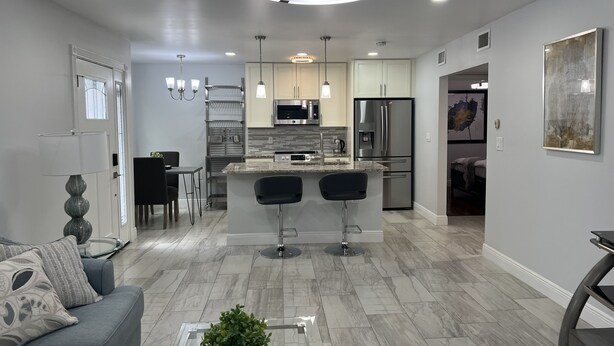 Una cucina moderna con isola centrale, elettrodomestici in acciaio inossidabile, luci a sospensione e un'area pranzo con divano e sedie.
