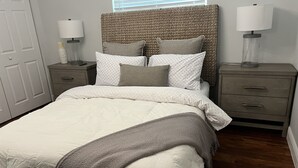 Una camera da letto con un letto grande, due comodini, un tavolino, una testiera intrecciata e una finestra con persiane.