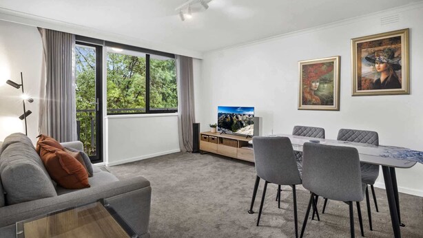 Ein modernes Wohnzimmer mit einer Couch, einem Esstisch mit Stühlen, einem Fernseher und zwei gerahmten Bildern an der Wand.