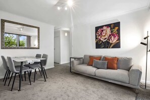 A modern living room with a dining area, a grey sofa with cushions, a large mirror, and a floral painting on the wall. - Comfortable Stay Near Melbourne’s West End (Ascot Vale)