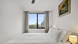 Ein Hotelzimmer mit einem großen Bett, einem Fenster mit Vorhängen, einem Gemälde an der Wand und einer Nachttischlampe.