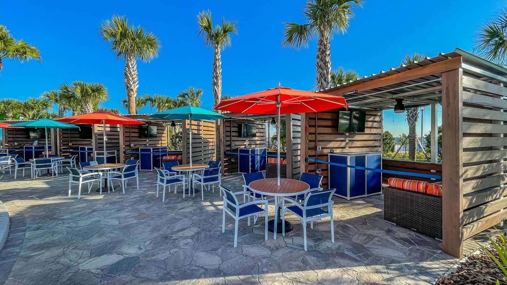 Un espace extérieur aménagé en terrasse, avec des tables et des chaises, des parasols et une structure en bois dotée de sièges.