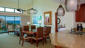 Habitación de hotel con zona de comedor, cocina, ventanas amplias y vista al océano.