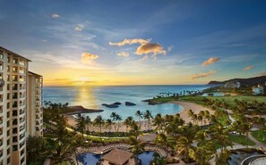 Ein Resort mit Poolbereich, Palmen und Blick auf den Ozean bei Sonnenuntergang.