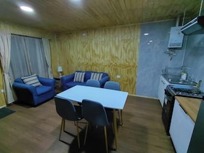 A room with a dining table, blue sofa, and a kitchenette.