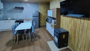 Una cocina compacta con comedor, microondas, refrigerador y televisor montado en la pared.