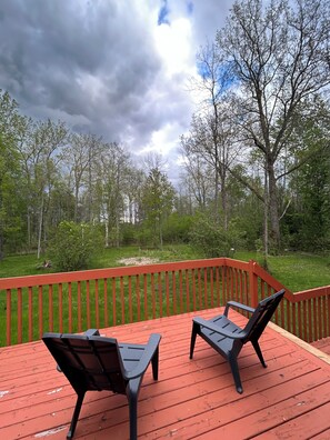 A wooden deck with two chairs and a railing, overlooking a forested area.
