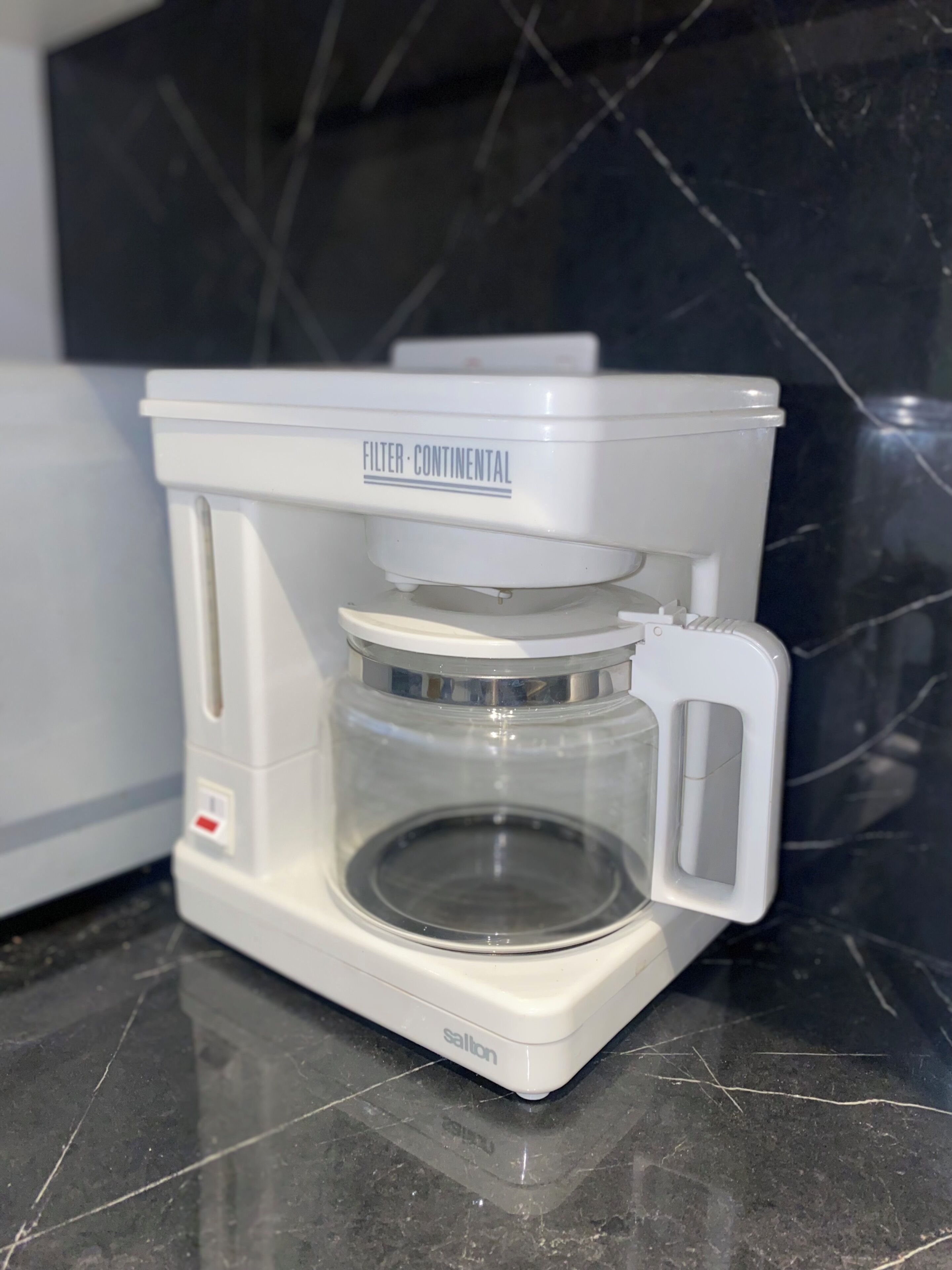 A coffee maker with a filter basket and a control panel, placed on a marble countertop.