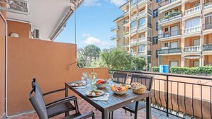 Ein Balkon mit Tisch, gedeckt für eine Mahlzeit, umgeben von einem Metallgeländer und mit Blick auf ein Wohngebäude.