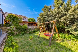 A residential property with a stone wall, a wooden swing set, and a garden with various plants.