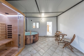 Un cuarto de sauna con un banco de madera, una mesa de madera con sillas y una bañera de hidromasaje con paredes de vidrio.