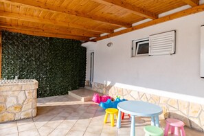 An outdoor patio area with a stone wall, a wooden ceiling, and a window with shutters.